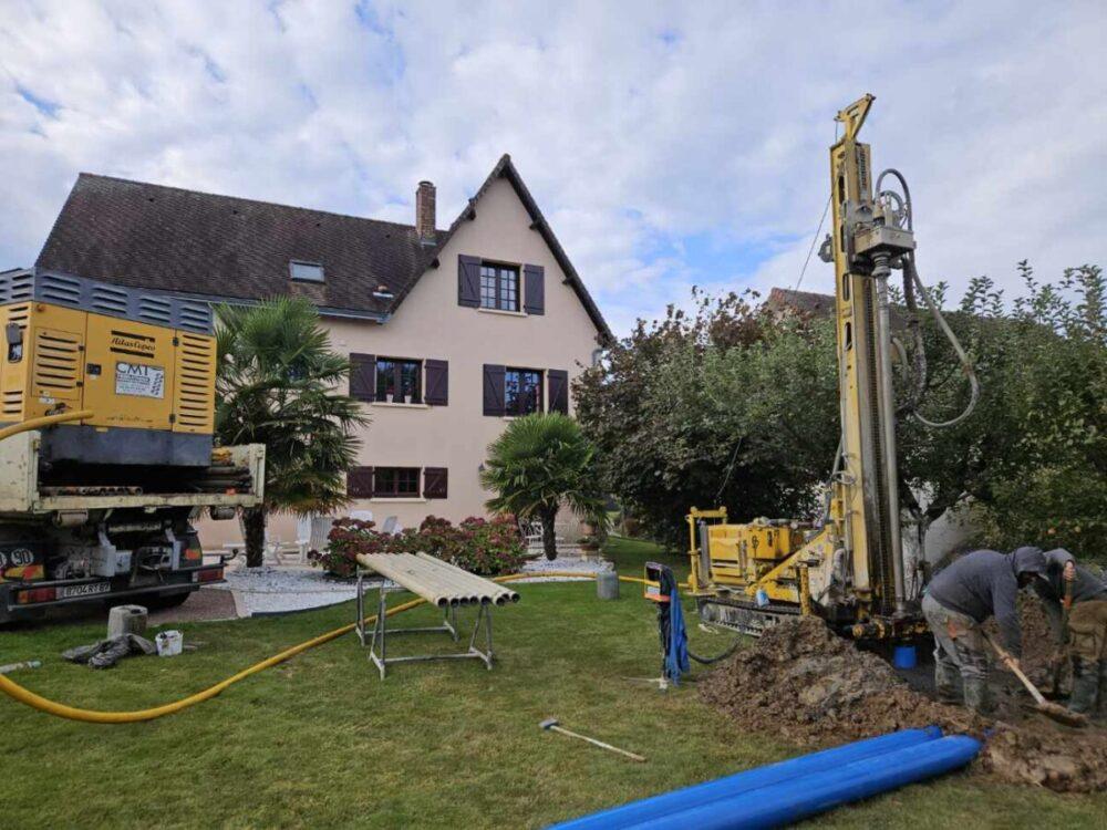 Chantier de forage avec une foreuse et un camion installés dans le jardin d'une maison