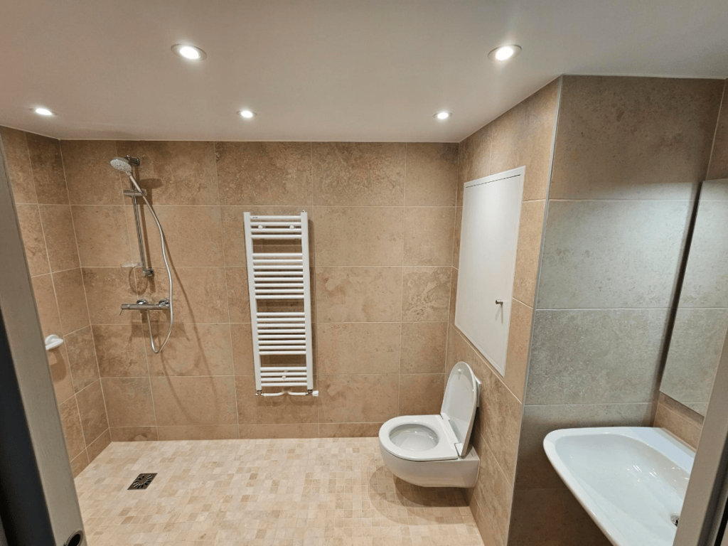 Salle de bain moderne en carrelage beige avec douche à l'italienne, sèche serviettes, WC suspendu et lavabo