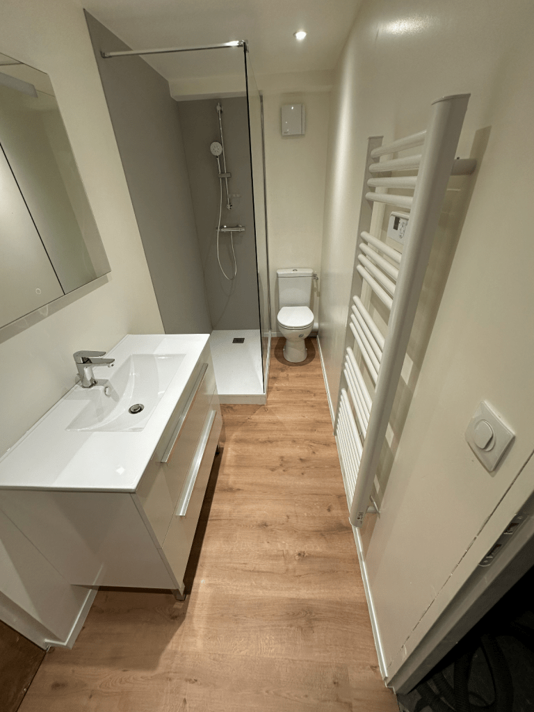 Salle de bains moderne avec meuble vasque blanc, douche à l'italienne vitrée, WC au fond et sèche-serviettes