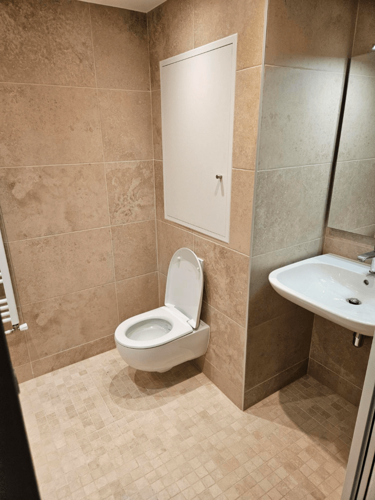Toilettes suspendues et lavabo dans une pièce carrelée de beige